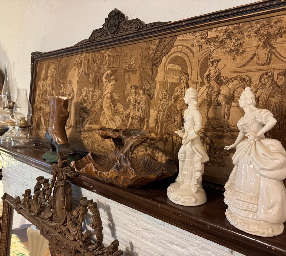 Ornate tapestry with porcelain figurines and oil lamp on a carved wood mantel